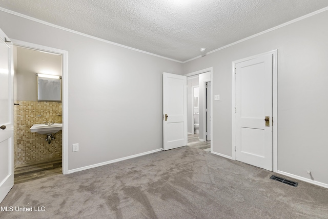 unfurnished bedroom with light carpet, a textured ceiling, connected bathroom, and crown molding