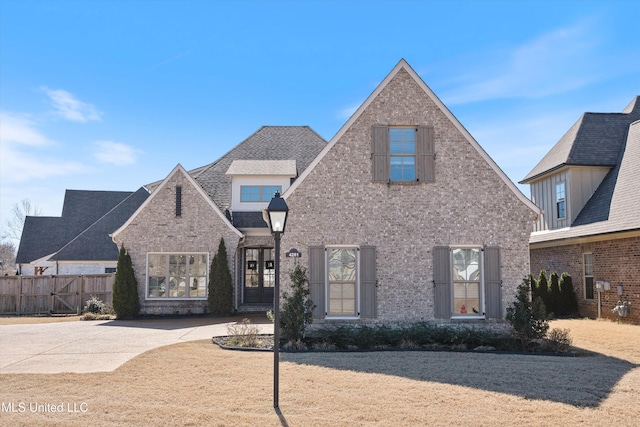 view of front of property featuring brick siding, roof with shingles, and fence