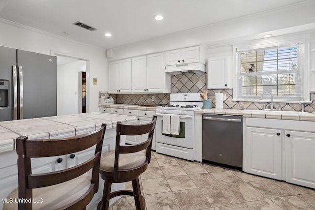 kitchen featuring under cabinet range hood, appliances with stainless steel finishes, white cabinets, and tile counters