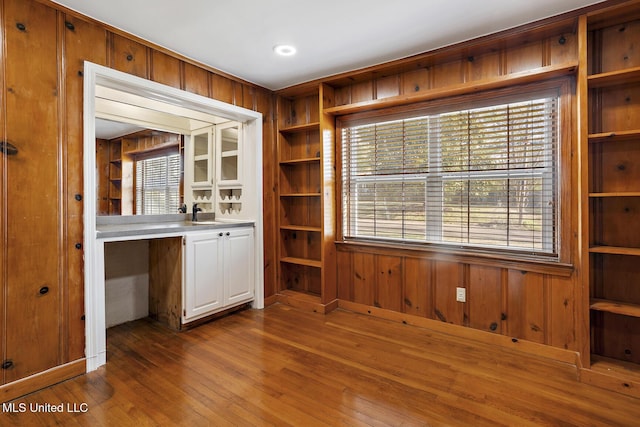 unfurnished office featuring a sink, wood walls, built in shelves, and hardwood / wood-style floors