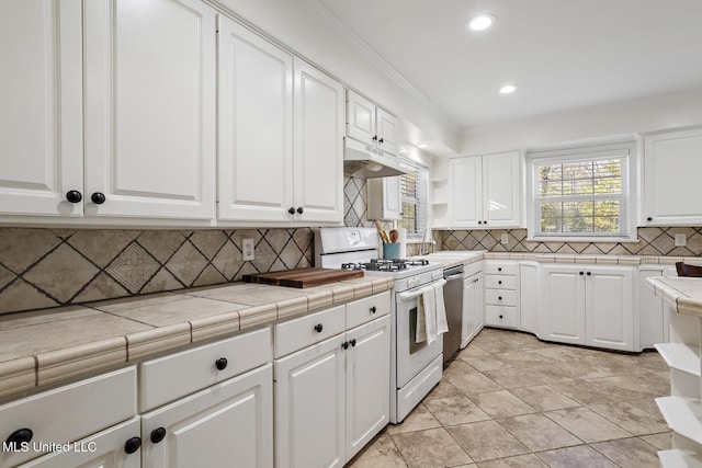 kitchen with white range with gas stovetop, tile counters, white cabinets, crown molding, and under cabinet range hood