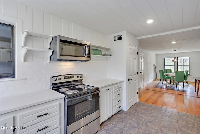 kitchen with decorative light fixtures, stainless steel appliances, white cabinetry, and light hardwood / wood-style flooring