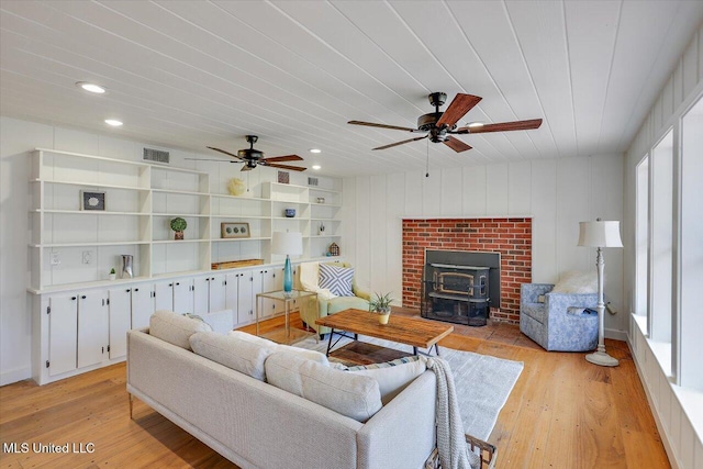 living room with a wood stove, wooden ceiling, ceiling fan, and light hardwood / wood-style floors