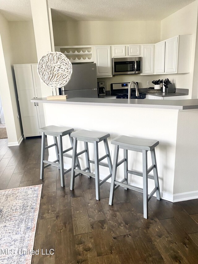 2252 Beach Dr Unit 203, Gulfport, MS 39507 - kitchen with appliances with stainless steel finishes, dark wood finished floors, white cabinets, and a breakfast bar