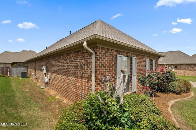 view of property exterior with roof with shingles, a lawn, brick siding, fence, and cooling unit