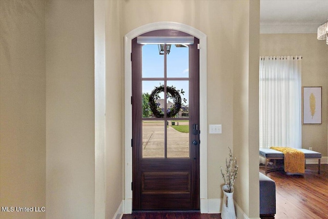 doorway to outside with arched walkways, a chandelier, baseboards, wood finished floors, and ornamental molding