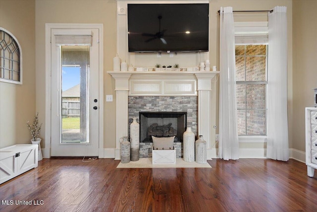 unfurnished living room featuring a tiled fireplace, baseboards, a ceiling fan, and wood finished floors