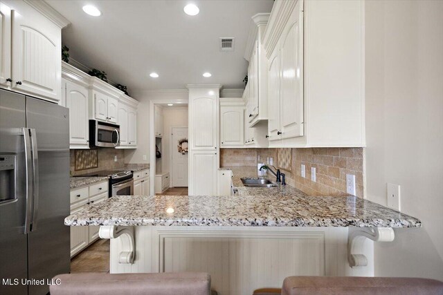 kitchen featuring visible vents, a peninsula, light stone countertops, a sink, and stainless steel appliances