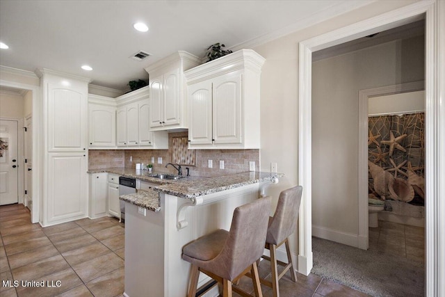 kitchen featuring dishwasher, a kitchen breakfast bar, light stone counters, a sink, and light tile patterned floors