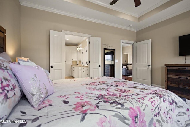 bedroom with crown molding, connected bathroom, a ceiling fan, baseboards, and a tray ceiling