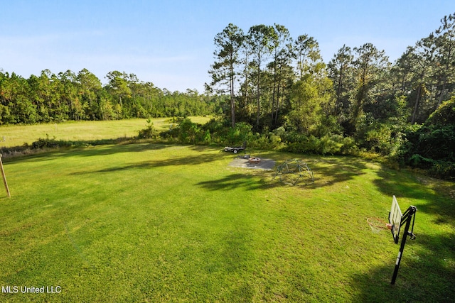 view of property's community featuring an outdoor fire pit, a view of trees, and a lawn