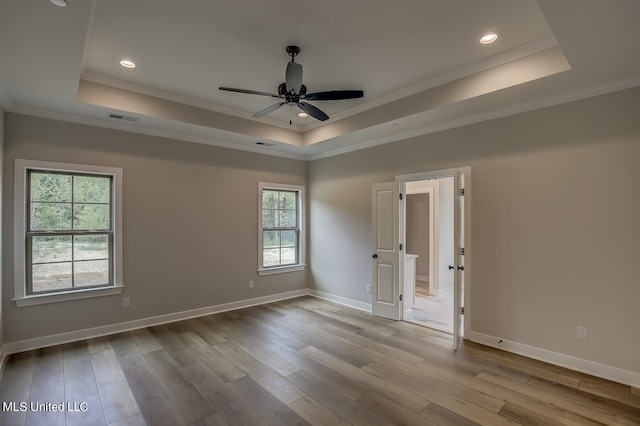 spare room featuring light hardwood / wood-style flooring, ornamental molding, ceiling fan, and a raised ceiling