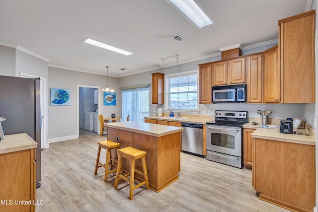 kitchen featuring sink, appliances with stainless steel finishes, ornamental molding, light hardwood / wood-style floors, and a kitchen island