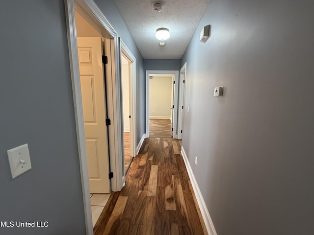 hall with a textured ceiling, dark wood-type flooring, and baseboards