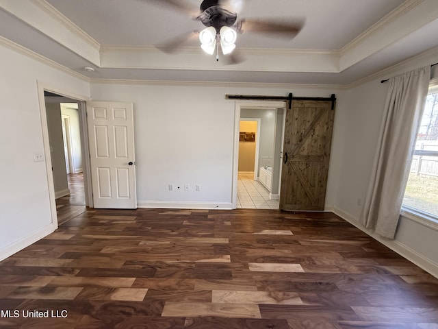 unfurnished bedroom with a barn door, multiple windows, and a raised ceiling