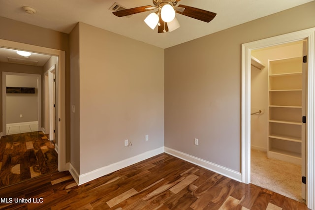 unfurnished bedroom featuring a walk in closet, visible vents, dark wood-type flooring, attic access, and baseboards