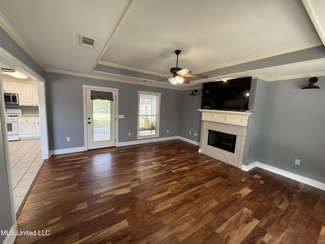 unfurnished living room with a tiled fireplace, visible vents, a tray ceiling, and wood finished floors