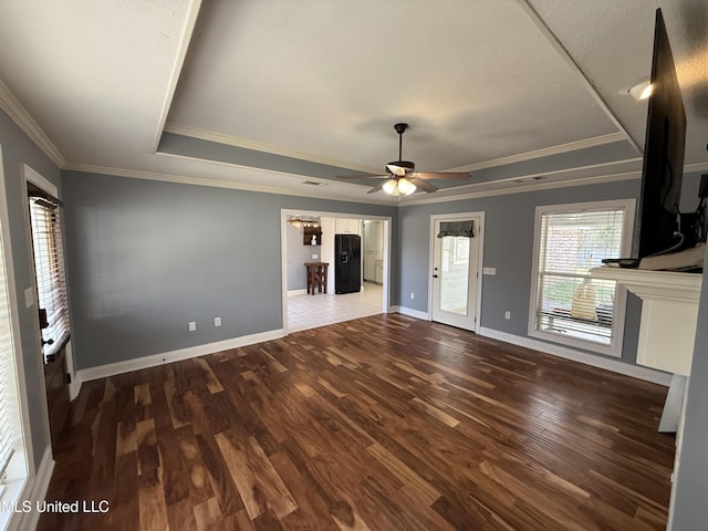 unfurnished living room featuring ceiling fan, wood finished floors, baseboards, ornamental molding, and a tray ceiling