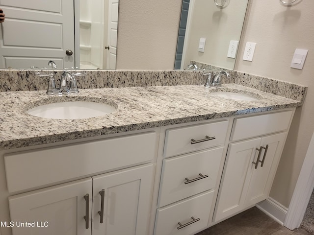 full bathroom featuring double vanity, baseboards, and a sink