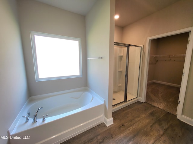 bathroom featuring a spacious closet, wood finished floors, a shower stall, and a bath