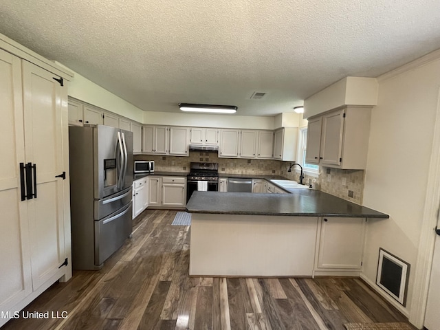 137 Phil Ln, Sardis, MS 38666 - kitchen featuring appliances with stainless steel finishes, a peninsula, dark wood-type flooring, dark countertops, and decorative backsplash