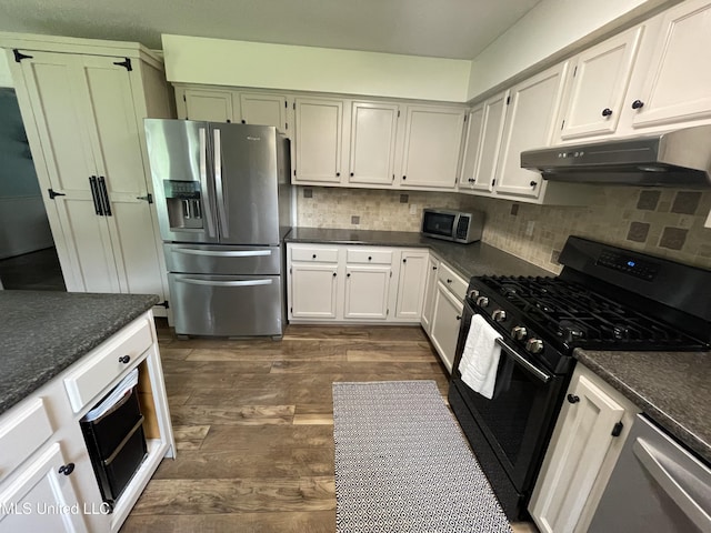 137 Phil Ln, Sardis, MS 38666 - kitchen with stainless steel appliances, under cabinet range hood, dark wood-type flooring, backsplash, and dark stone countertops