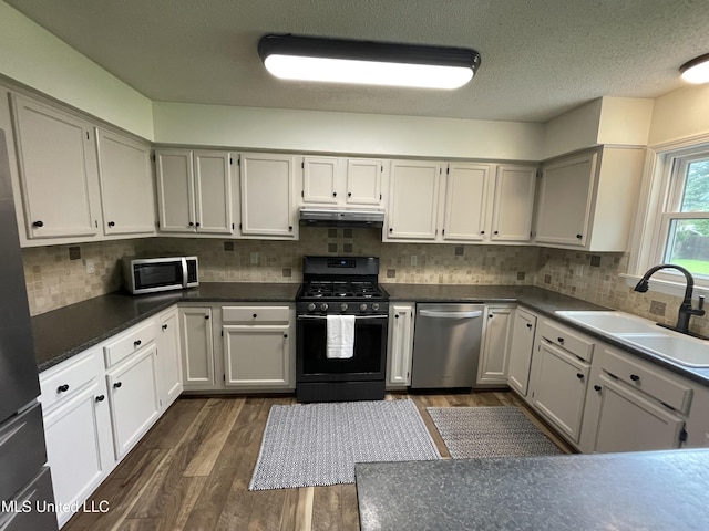 137 Phil Ln, Sardis, MS 38666 - kitchen with appliances with stainless steel finishes, under cabinet range hood, dark wood-type flooring, decorative backsplash, and dark countertops