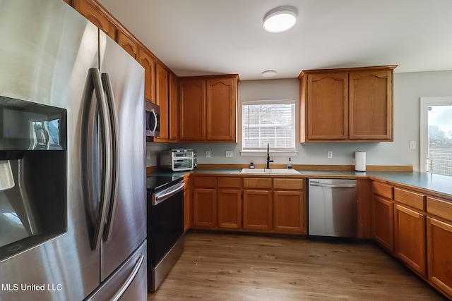 kitchen with light wood-type flooring, brown cabinetry, stainless steel appliances, and a sink