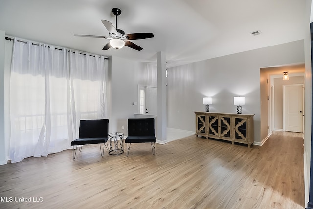 living area featuring light wood finished floors, baseboards, and a ceiling fan