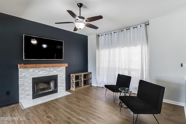 sitting room with a fireplace, wood finished floors, a ceiling fan, and baseboards