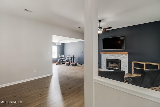 living room featuring a fireplace, visible vents, a ceiling fan, wood finished floors, and baseboards