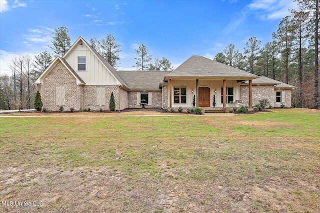 view of front facade with brick siding, roof with shingles, covered porch, board and batten siding, and a front yard