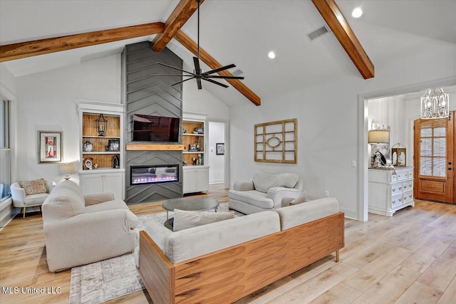 living room featuring light wood-style flooring, visible vents, beamed ceiling, and a glass covered fireplace