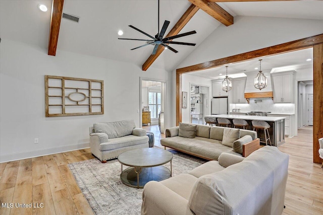 living room with visible vents, beamed ceiling, ceiling fan with notable chandelier, and light wood-style flooring