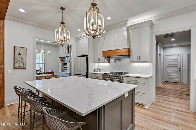 kitchen with light stone counters, a center island, freestanding refrigerator, high end stainless steel range oven, and premium range hood