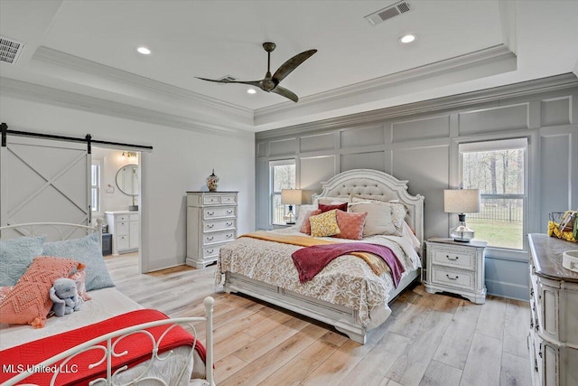 bedroom with a barn door, a decorative wall, visible vents, a raised ceiling, and crown molding