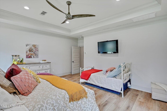 bedroom featuring light wood-style floors, visible vents, a raised ceiling, and crown molding