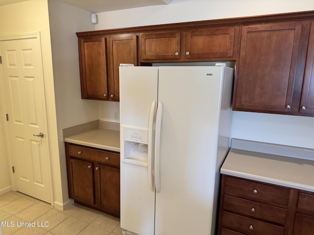 kitchen featuring white refrigerator with ice dispenser, light tile patterned floors, and light countertops