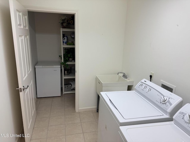clothes washing area featuring washing machine and dryer, light tile patterned floors, and baseboards