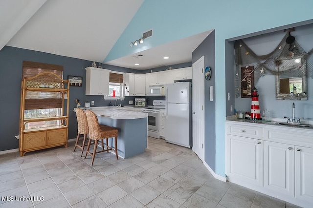 kitchen featuring white appliances, lofted ceiling, a kitchen breakfast bar, sink, and white cabinetry