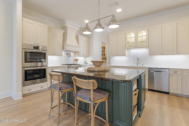 kitchen with a sink, a kitchen island, visible vents, appliances with stainless steel finishes, and custom exhaust hood