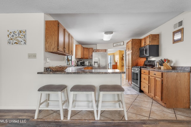 kitchen featuring a kitchen bar, light tile patterned floors, a textured ceiling, and stainless steel appliances