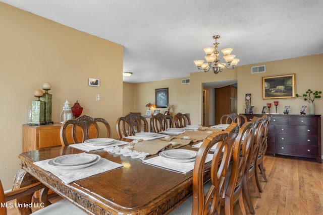 dining area featuring light wood-type flooring, a textured ceiling, and a chandelier