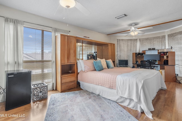 bedroom with a textured ceiling, light hardwood / wood-style flooring, multiple windows, and ceiling fan