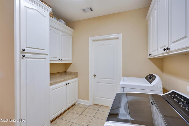 clothes washing area featuring light tile patterned floors, washing machine and dryer, and cabinets