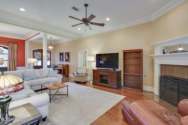 living room with hardwood / wood-style floors, a fireplace, decorative columns, ceiling fan, and crown molding