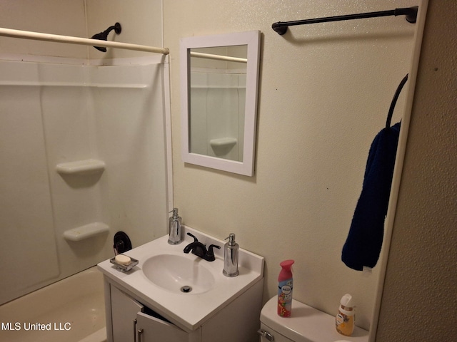 bathroom with toilet, vanity, a textured wall, and washtub / shower combination