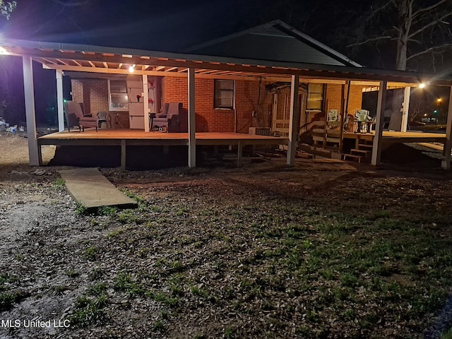 back of house at twilight featuring brick siding, a wooden deck, and a pergola