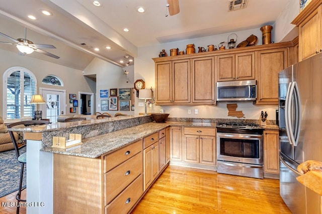 kitchen featuring stainless steel appliances, light stone countertops, kitchen peninsula, a kitchen bar, and lofted ceiling