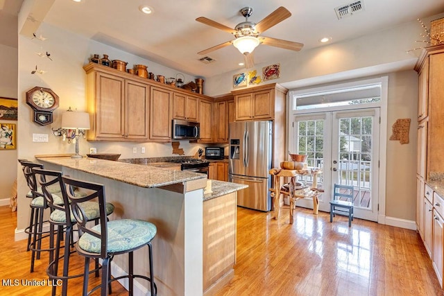 kitchen with stainless steel appliances, french doors, kitchen peninsula, a breakfast bar area, and light stone countertops